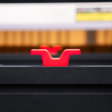 A close-up shot of a bright red plastic mounting bracket or handle attached to a black metal surface, with a blurred background showing warm orange and white tones.