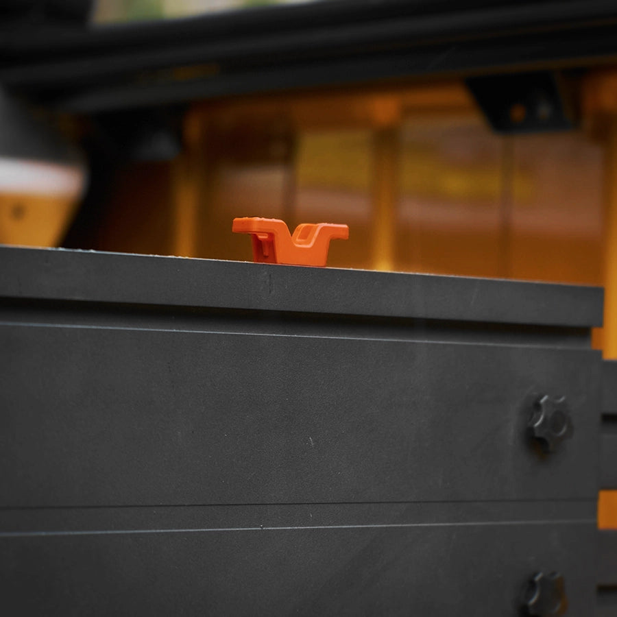 A close-up shot of a bright red plastic mounting bracket or handle attached to a black metal surface, with a blurred background showing warm orange and white tones.